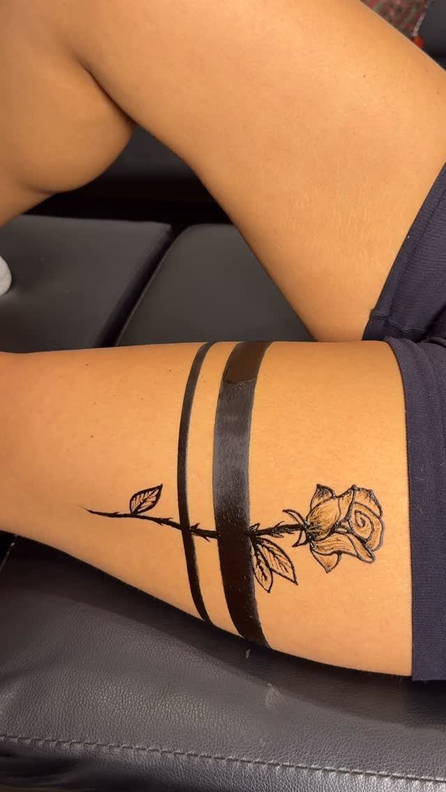 Rose tattoo with black bands on a person's upper thigh