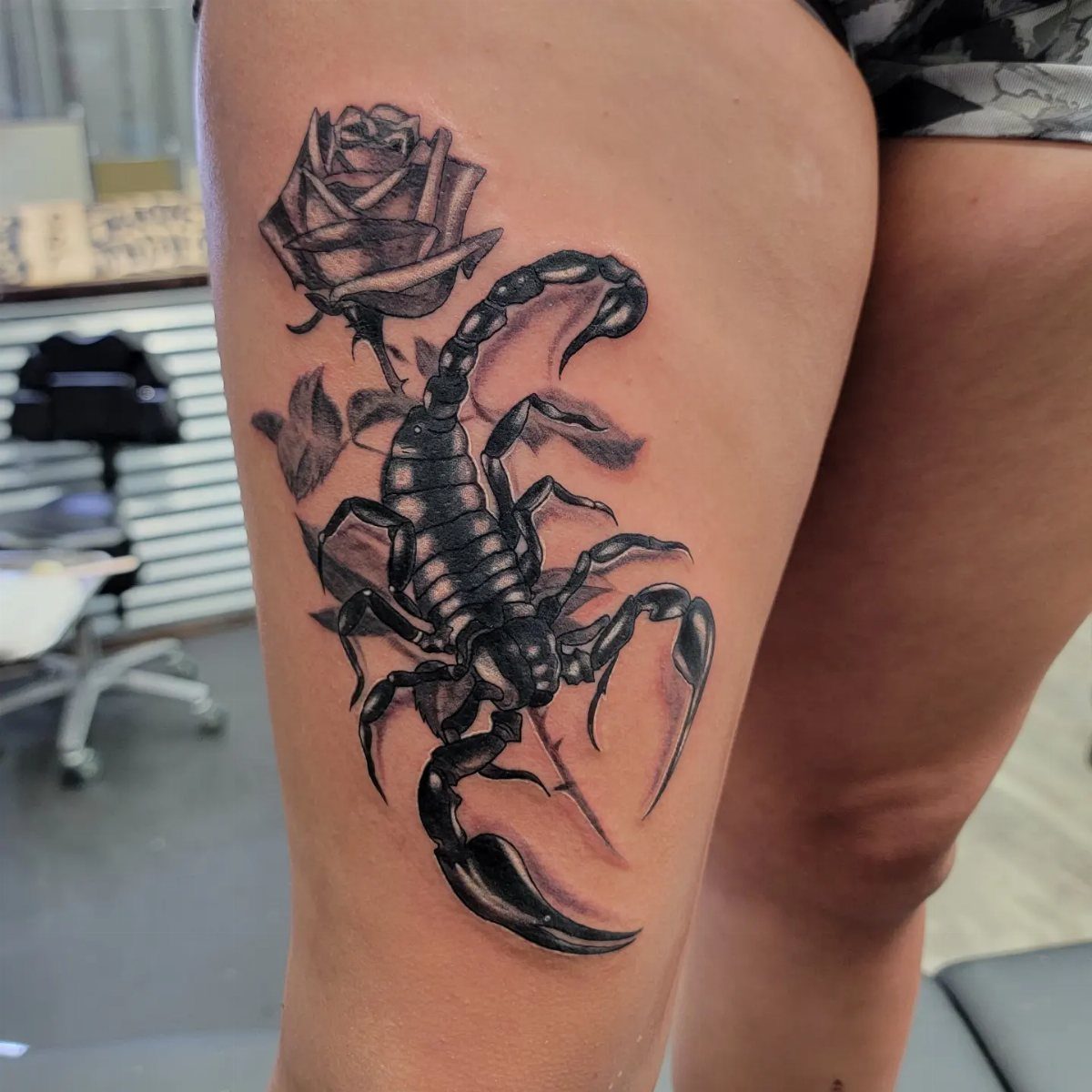 Scorpion and rose tattoo on the upper leg of a person.
