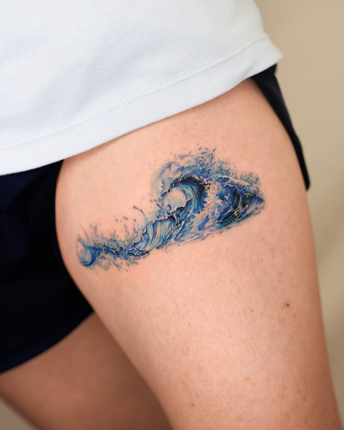 Blue watercolor ocean wave tattoo on a person's upper thigh.