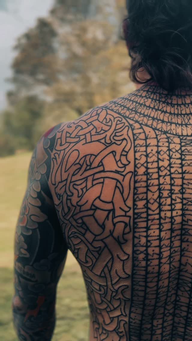 Man's back with intricate Celtic knotwork and geometric black ink tattoos outdoors