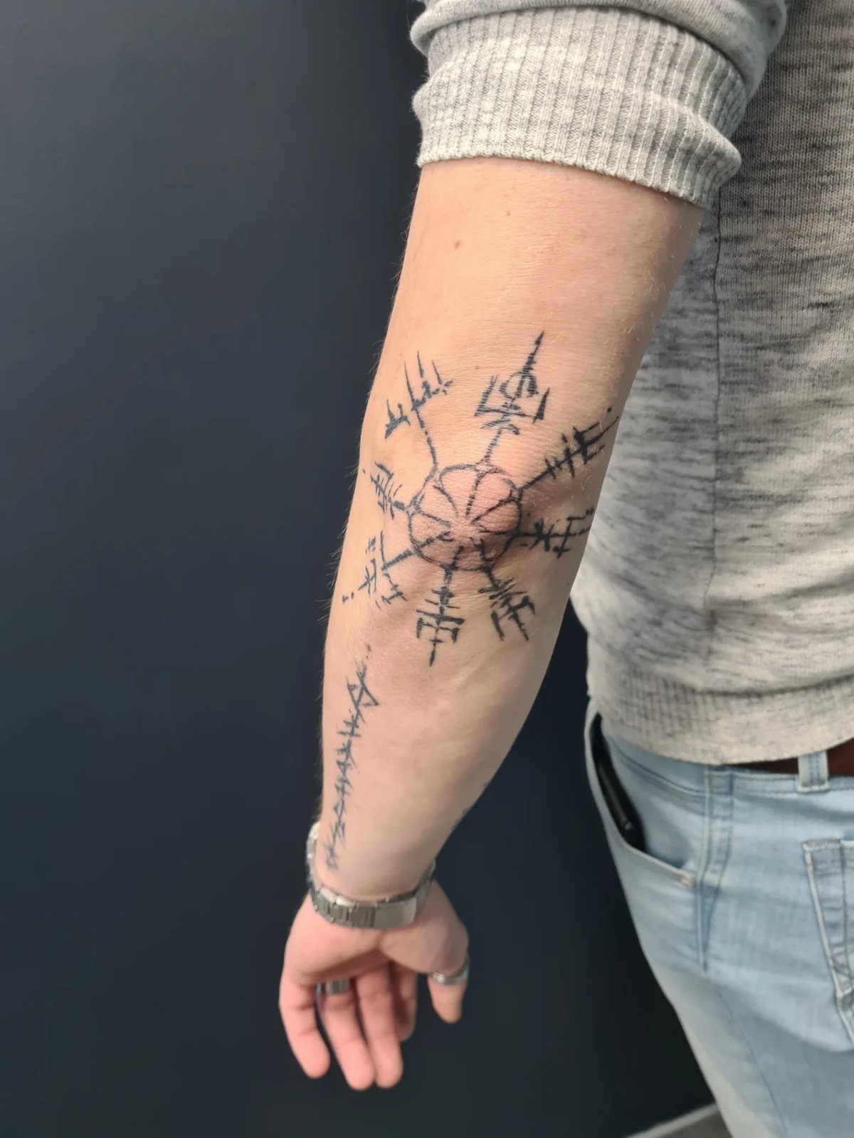 Vegvisir tattoo on a man's forearm with accompanying Norse runes in black ink.