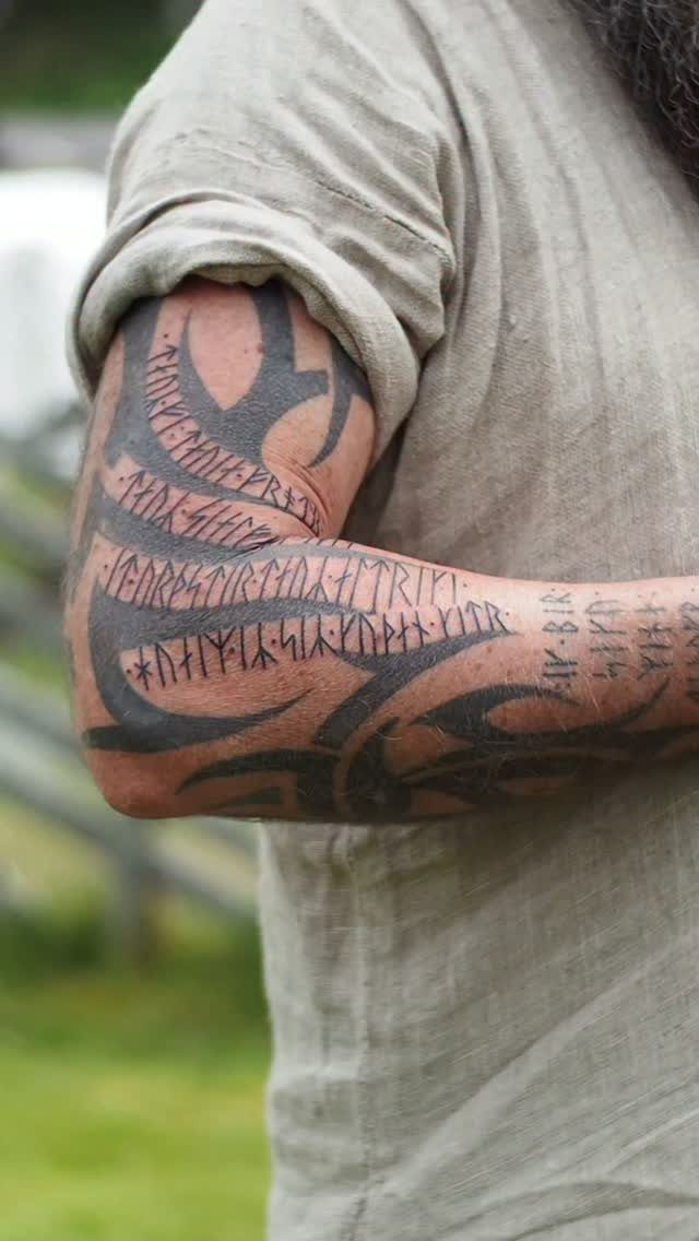 Man's arm with black ink Viking runes and tribal tattoos wearing linen clothing