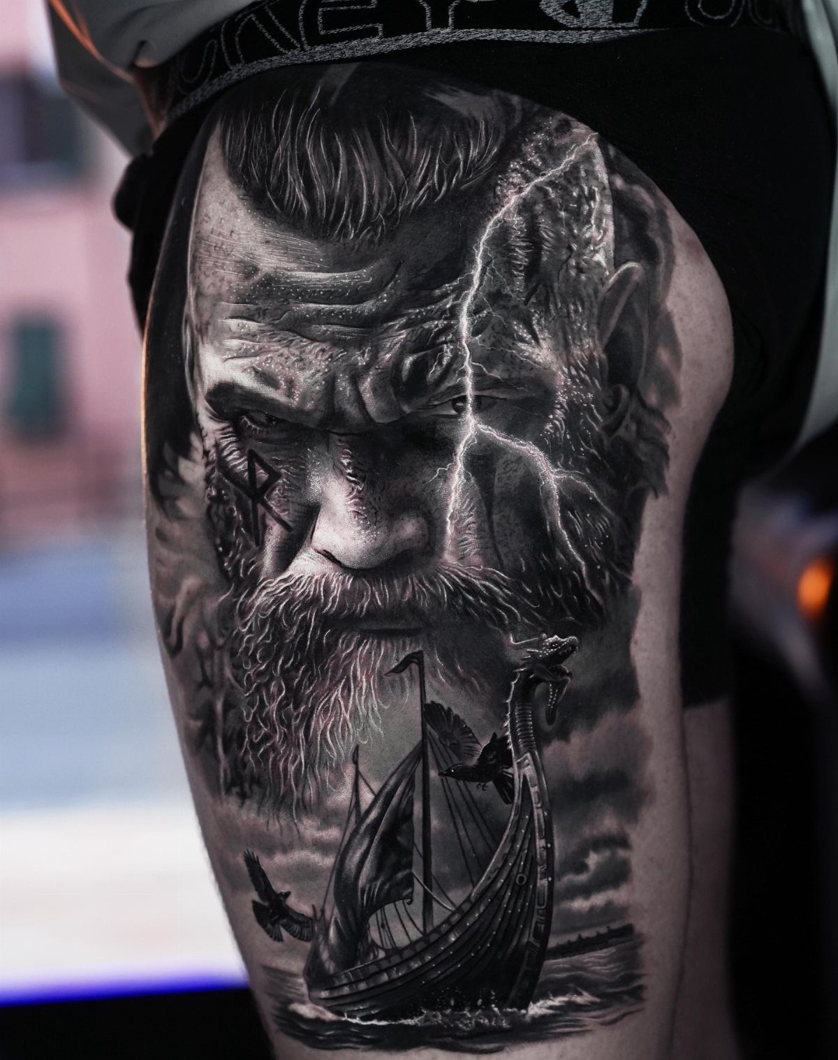 Viking warrior face and longship tattoo in black and grey realism on a thigh