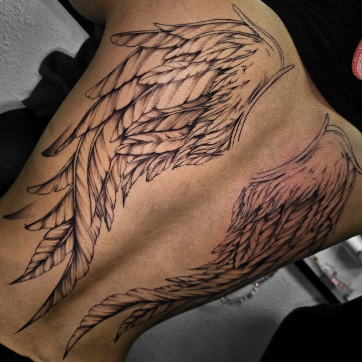 Symmetrical feathered wing tattoos on a person's back with detailed black ink shading.