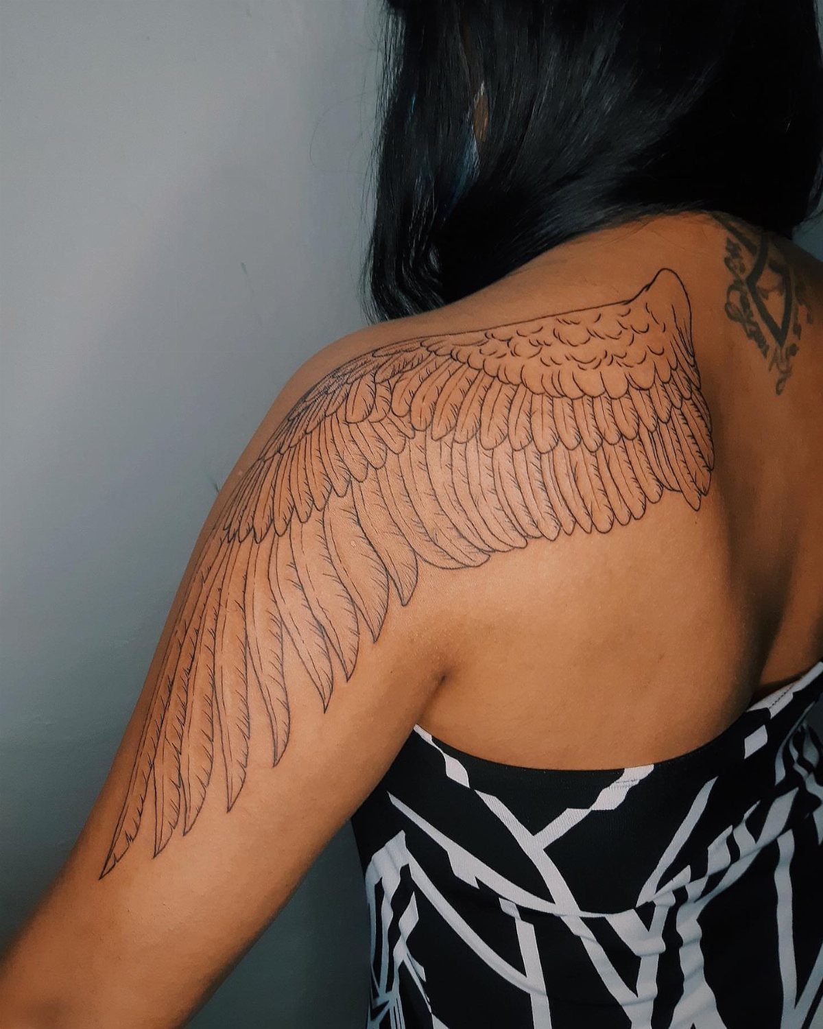 Feathered wing tattoo extending from the upper back down the person's arm.