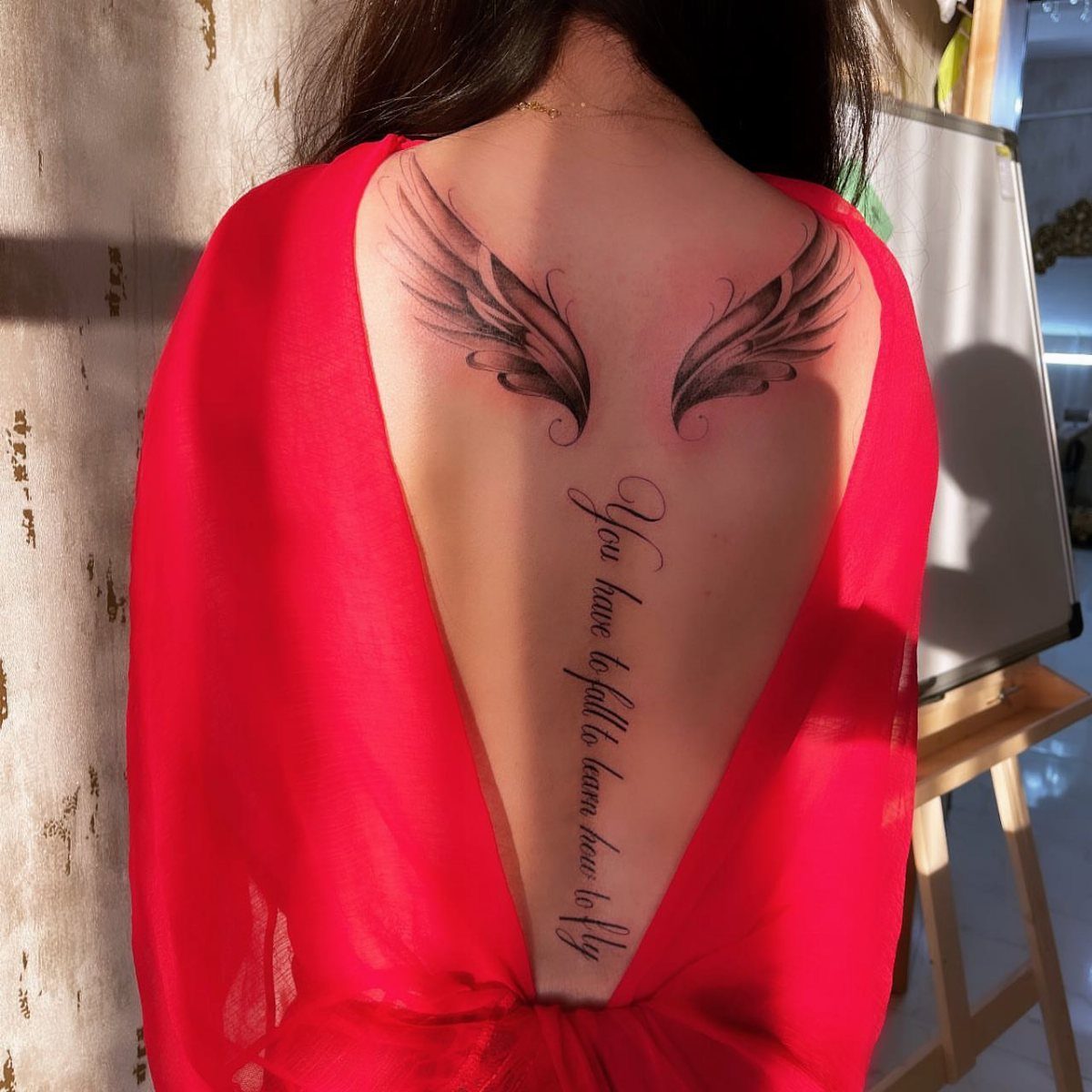Tattoo of black feathered wings and a cursive quote on a person's back.