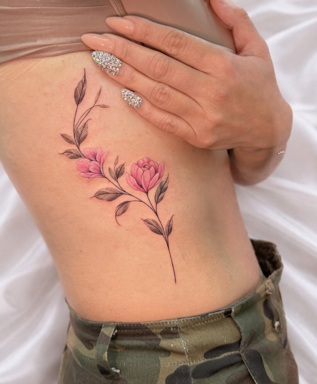 Pink flower tattoo with black stems on a woman's side torso