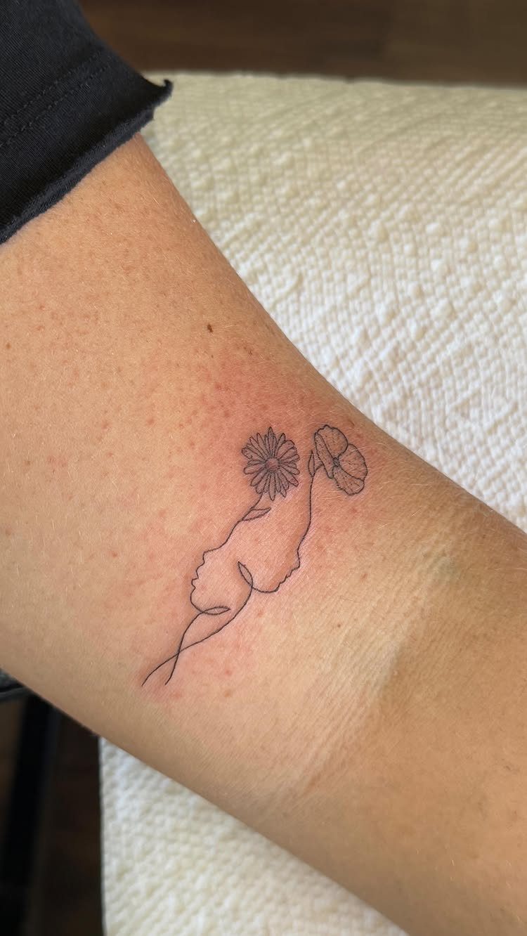 Minimalist flower outline tattoo featuring a face profile and blossoms on an arm.