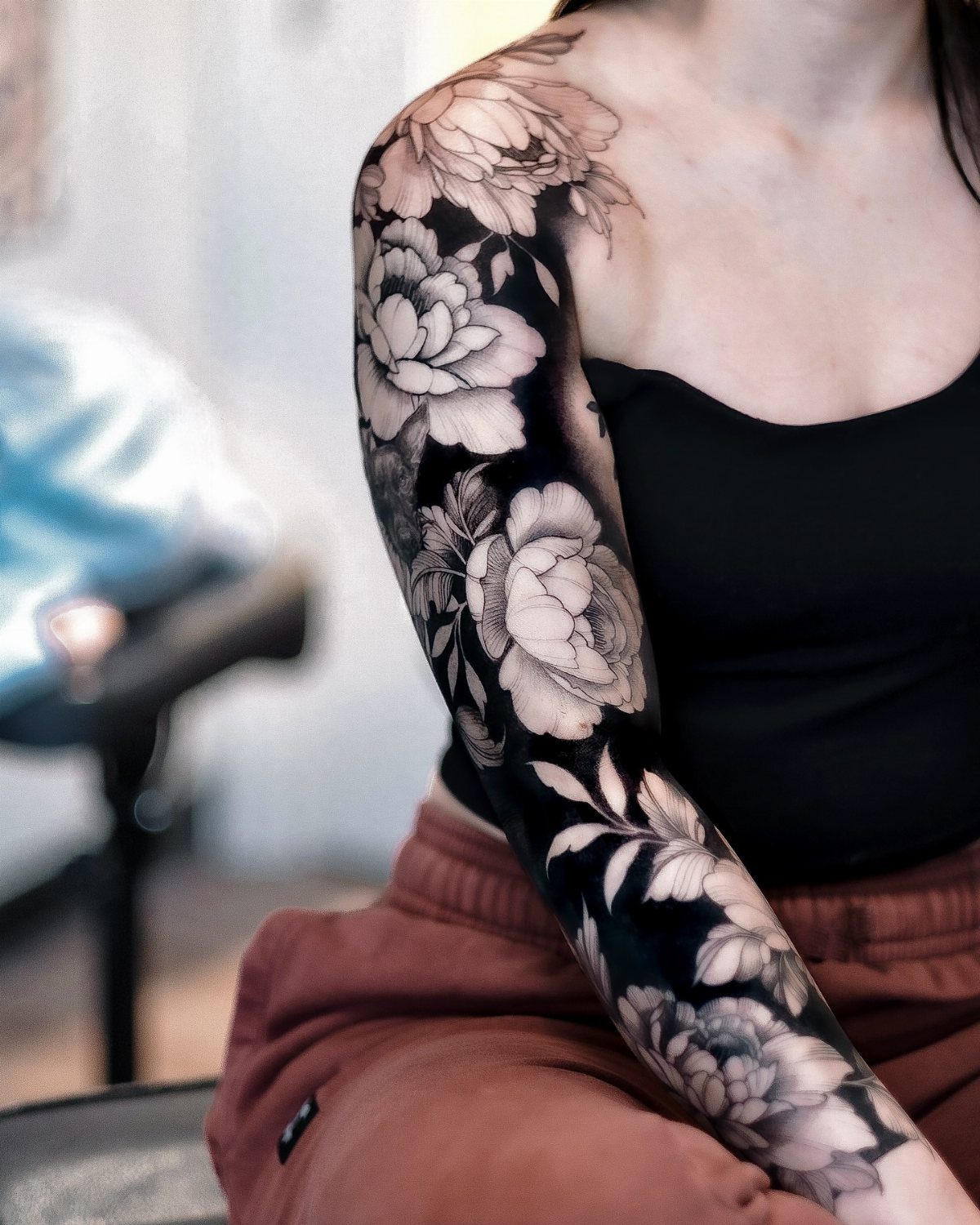 Woman's arm with a full sleeve tattoo of realistic black and grey flowers.