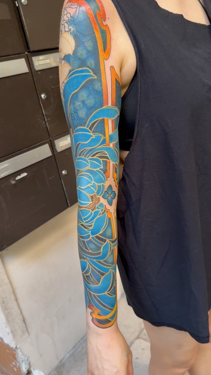 Full sleeve tattoo of blue chrysanthemums and flowing water on a person's arm.