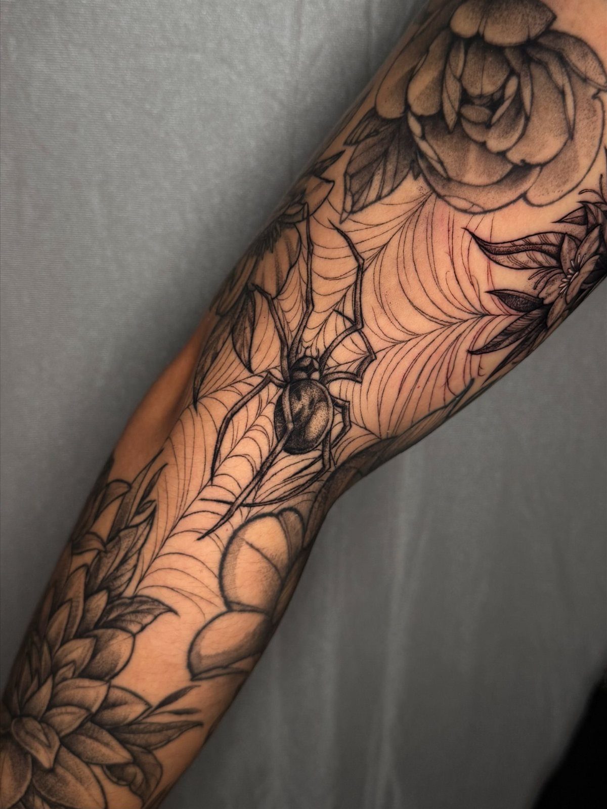Tattoo sleeve with a large spider in a web and grey roses.