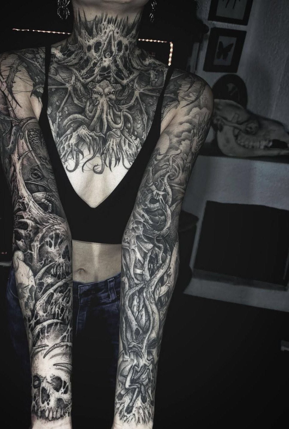 Woman with full sleeve blackwork tattoos featuring skulls and dark surreal imagery.