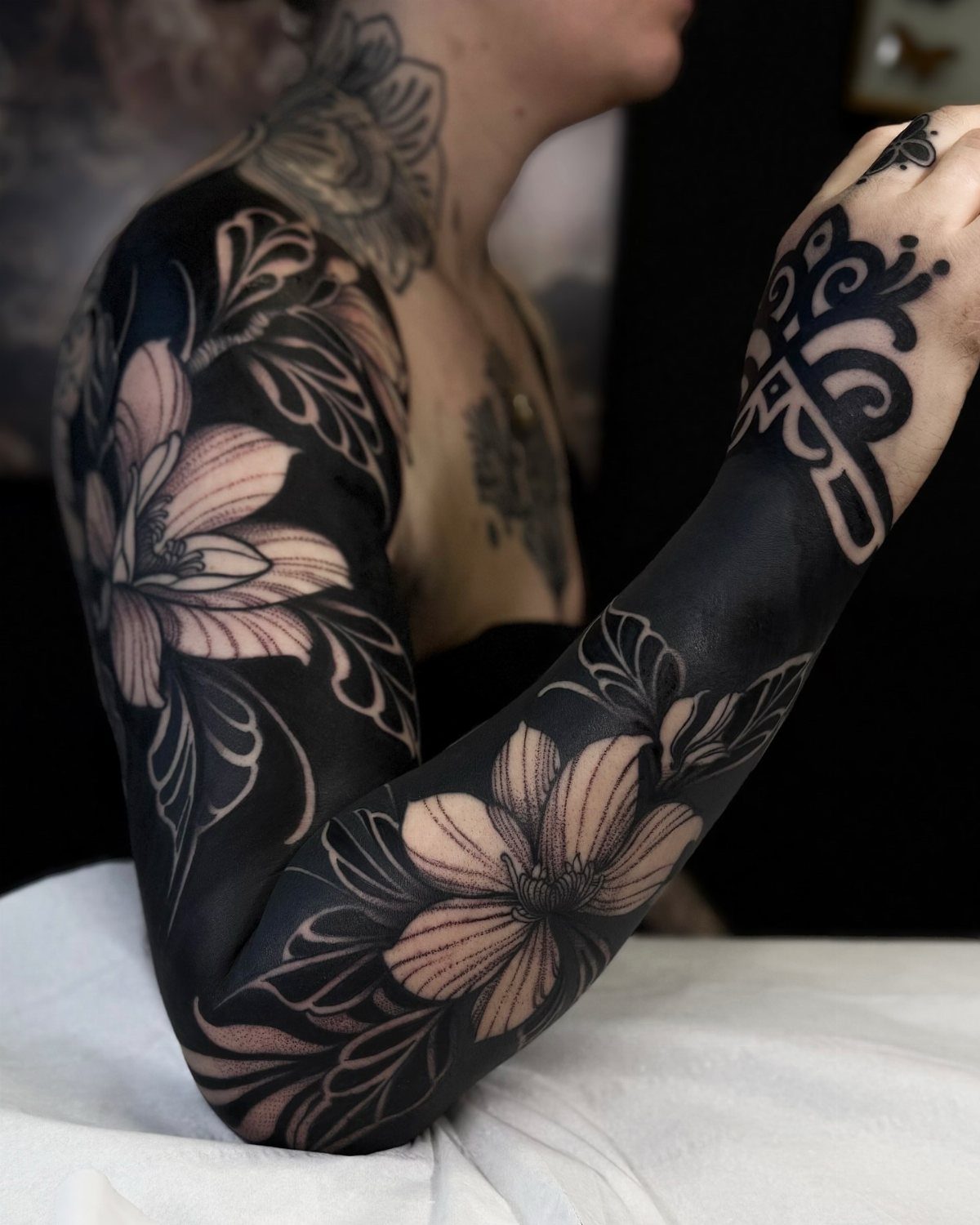 Full sleeve tattoo with illustrative flowers and ornamental patterns on a black background.