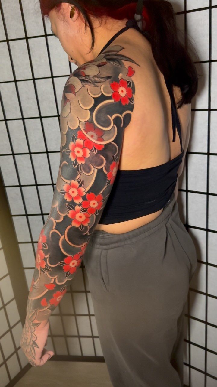 Woman's arm with a Japanese sleeve tattoo of dark waves and red flowers.
