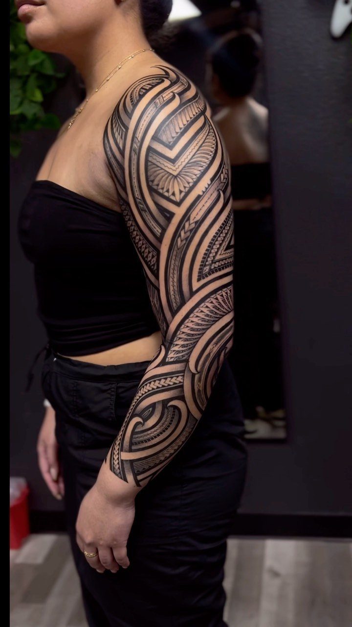 Woman with a full sleeve tribal tattoo featuring bold black geometric linework patterns.