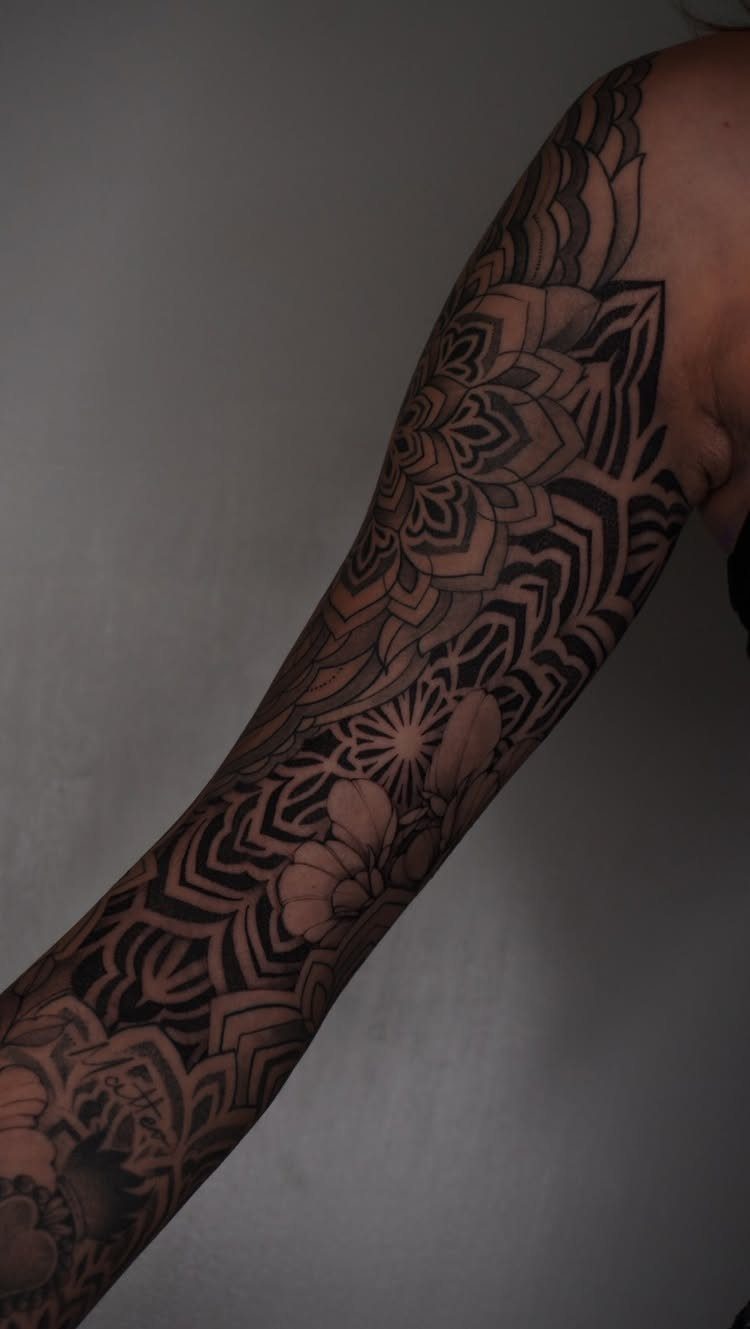 Full sleeve tattoo with black ornamental mandalas and geometric patterns on an arm.
