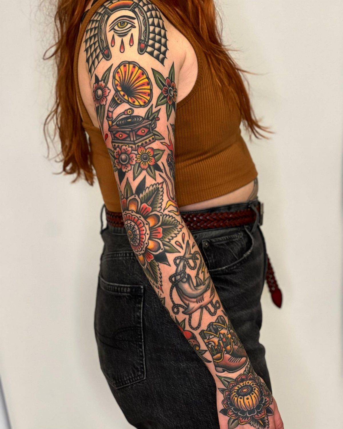 Woman with red hair showing a colorful traditional style full sleeve tattoo.