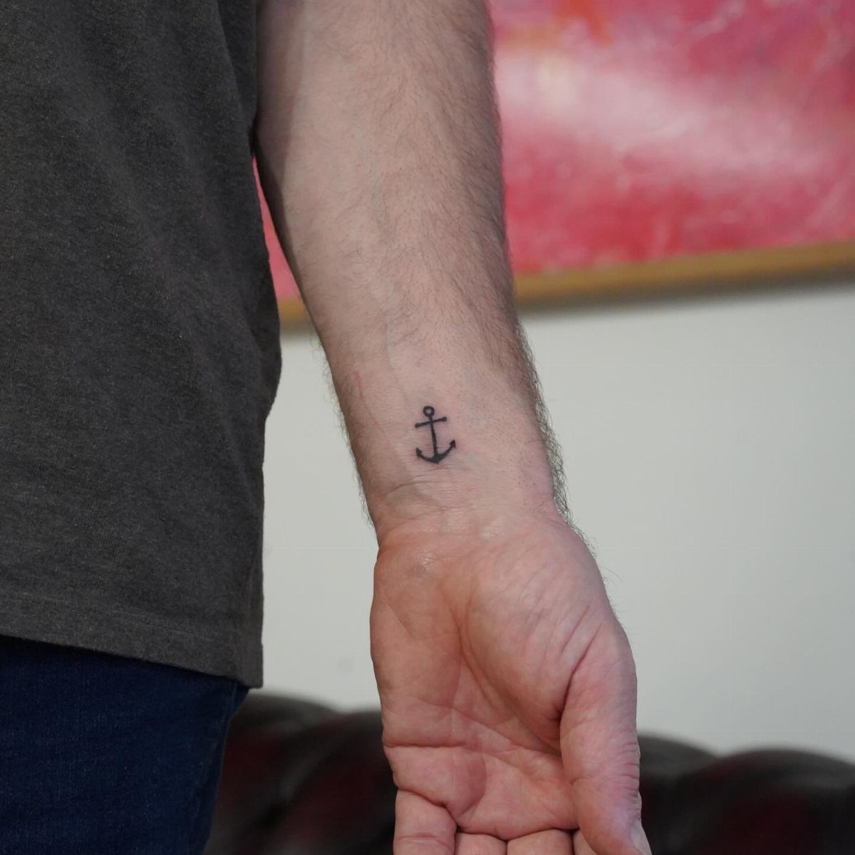 Small black anchor tattoo on the inner wrist of a man's arm.