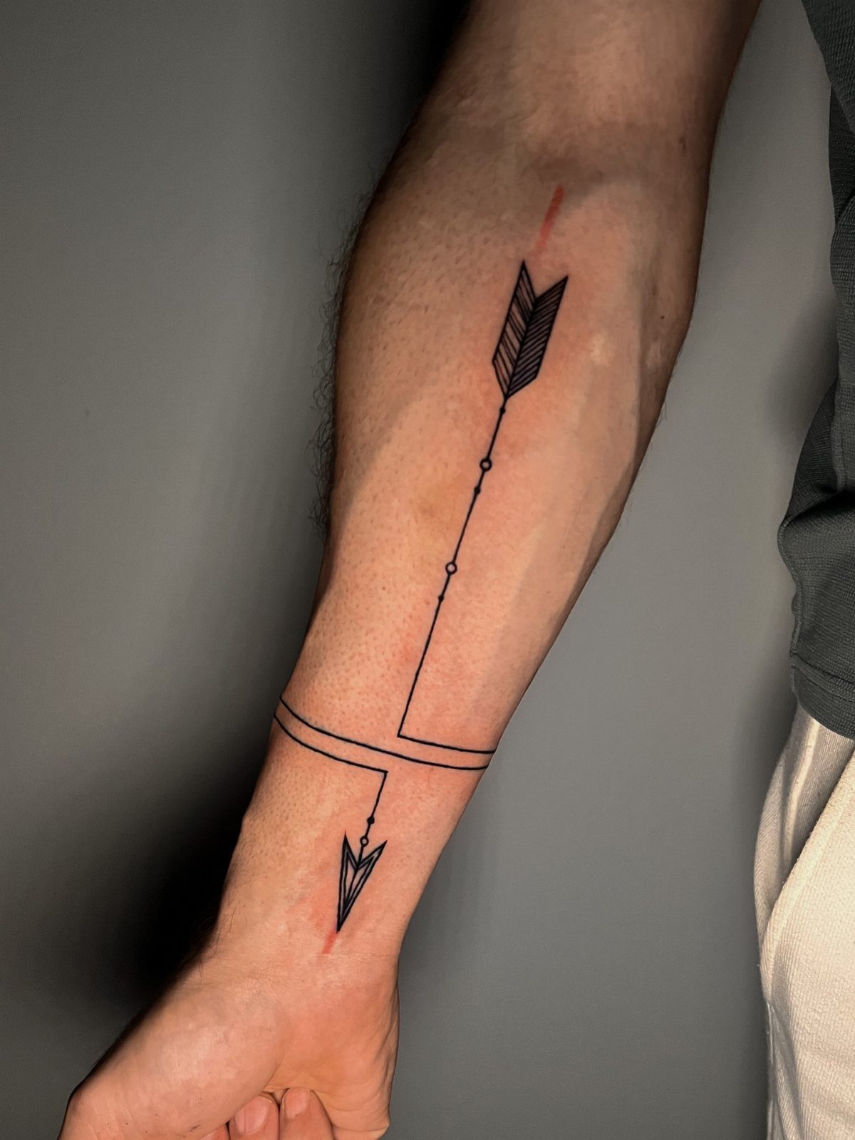 Black ink arrow tattoo extending down a forearm to the wrist with a band.