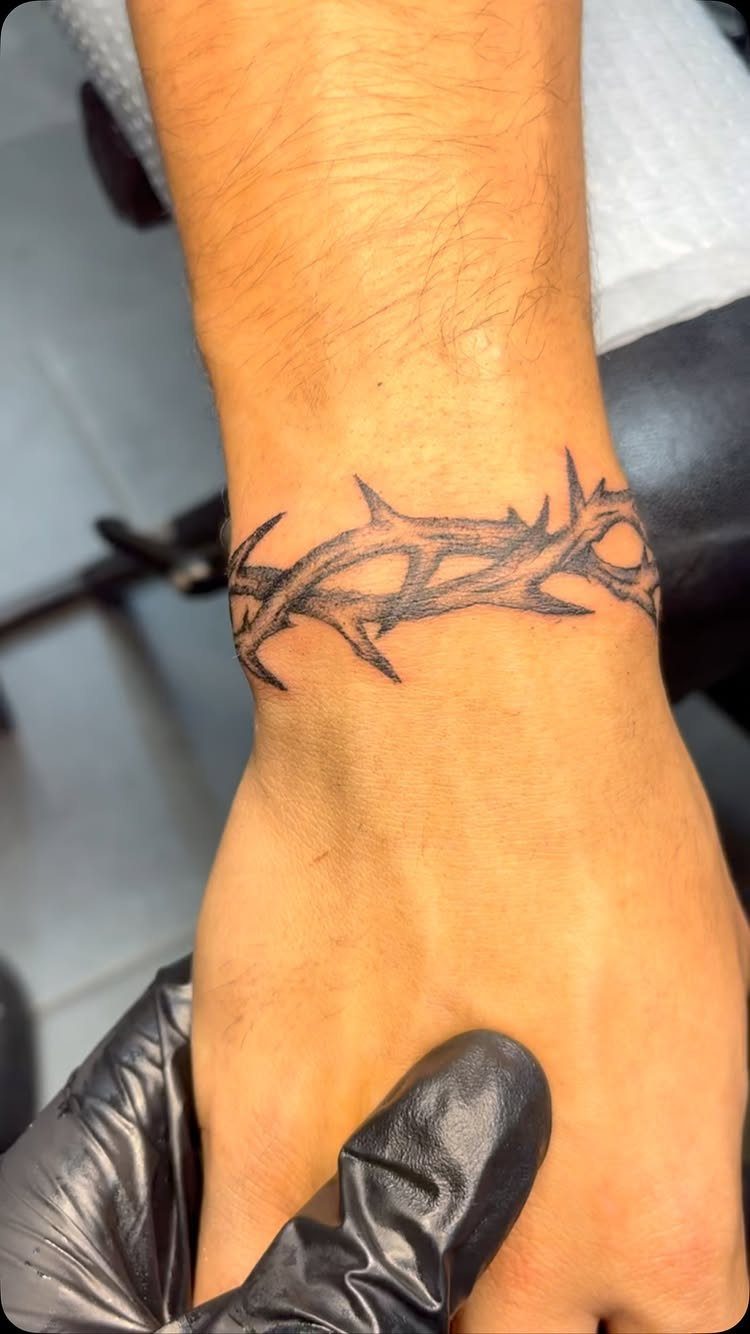 Wrist tattoo of a black thorny vine wrapping around a man's arm.