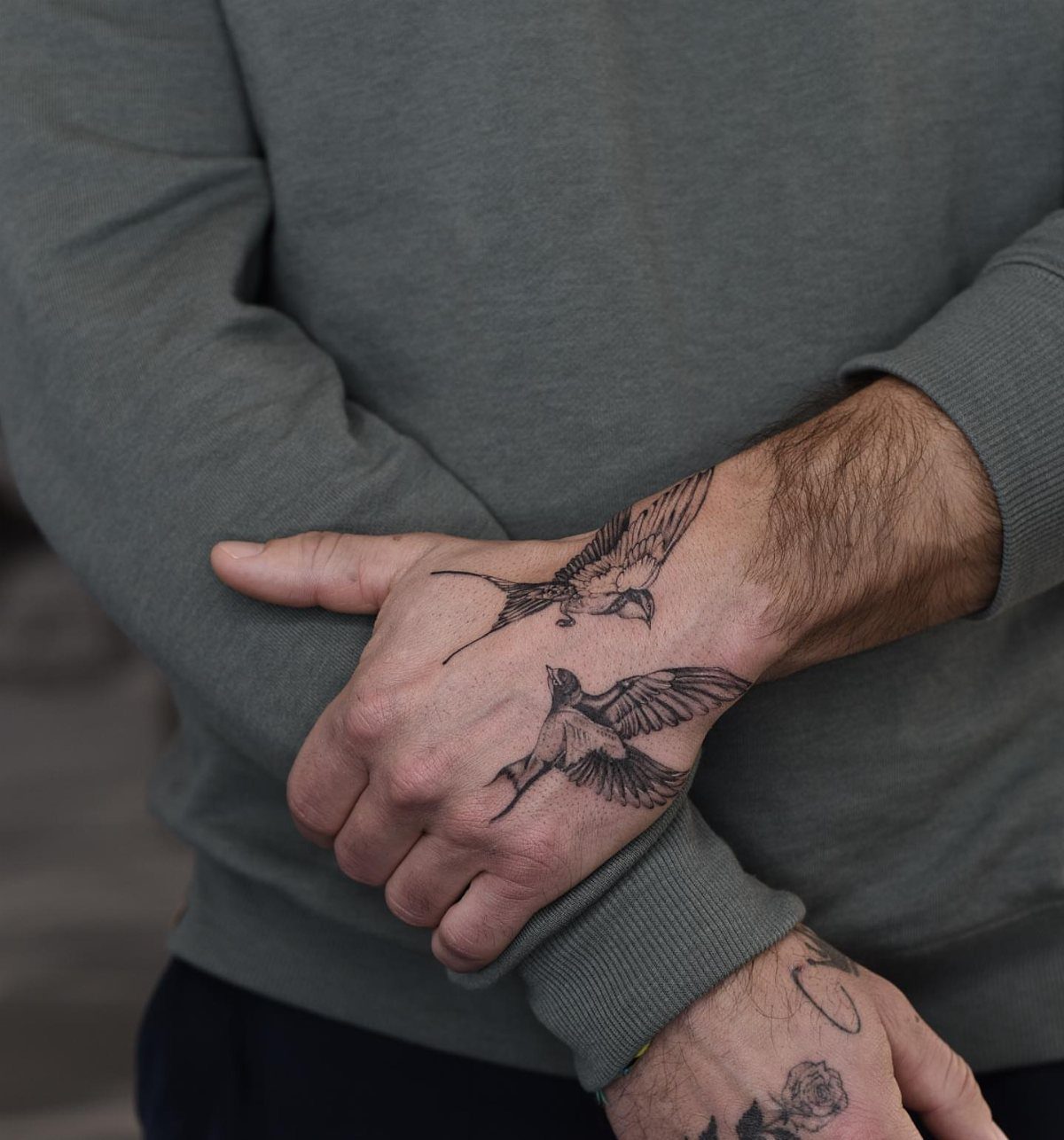 Two black swallow bird tattoos on a man's wrist and hand