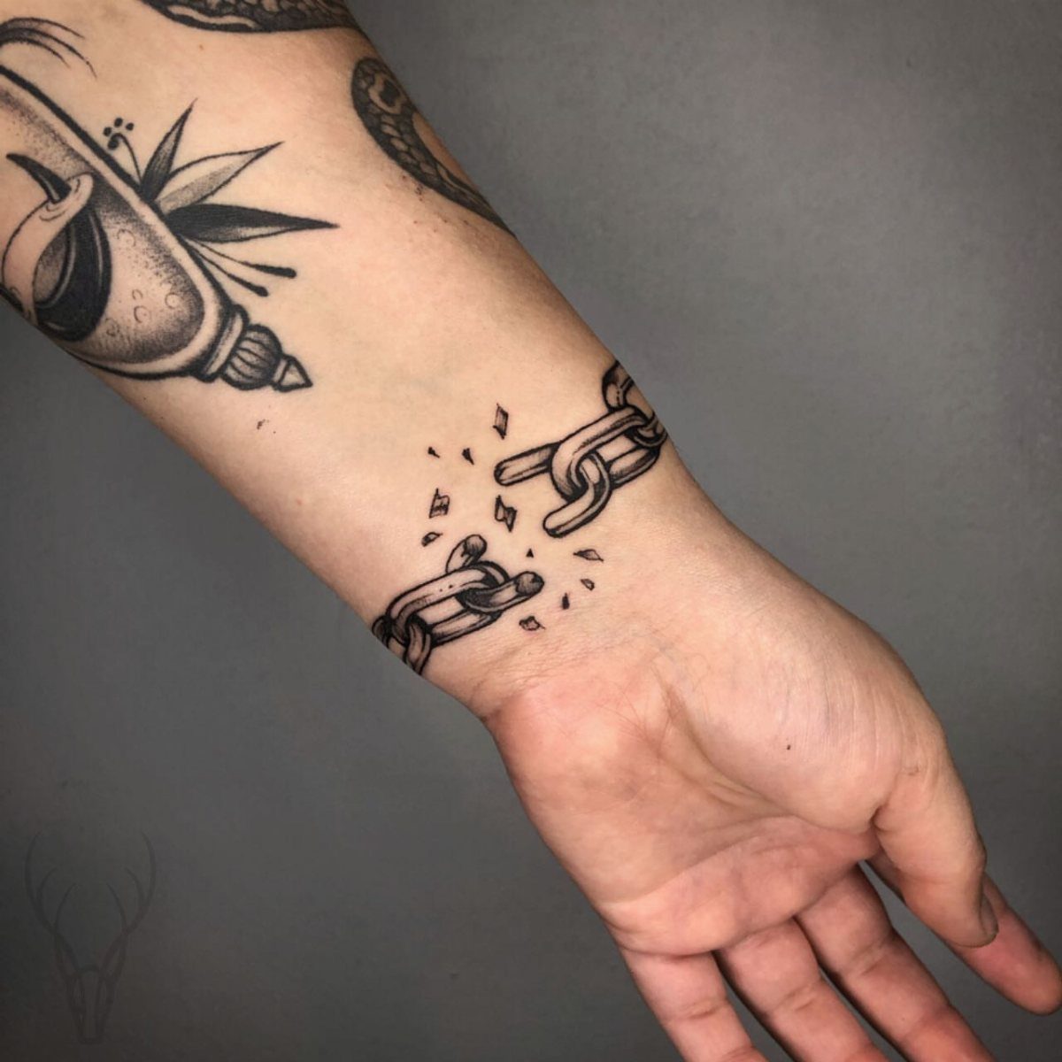 Broken chain tattoo on a wrist with small fragments between the severed links.