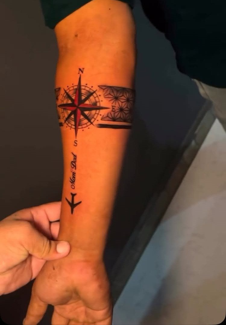 Compass rose tattoo on a man's forearm with an airplane and text.