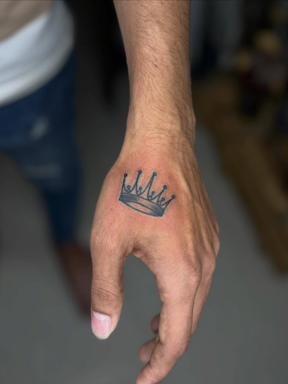 Hand with a small black ink crown tattoo on the back of the wrist.