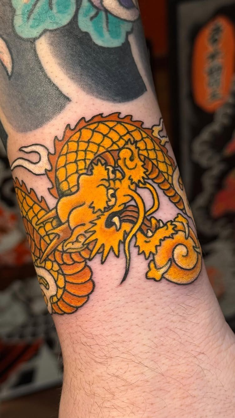 Orange and yellow dragon tattoo on a person's wrist and forearm.