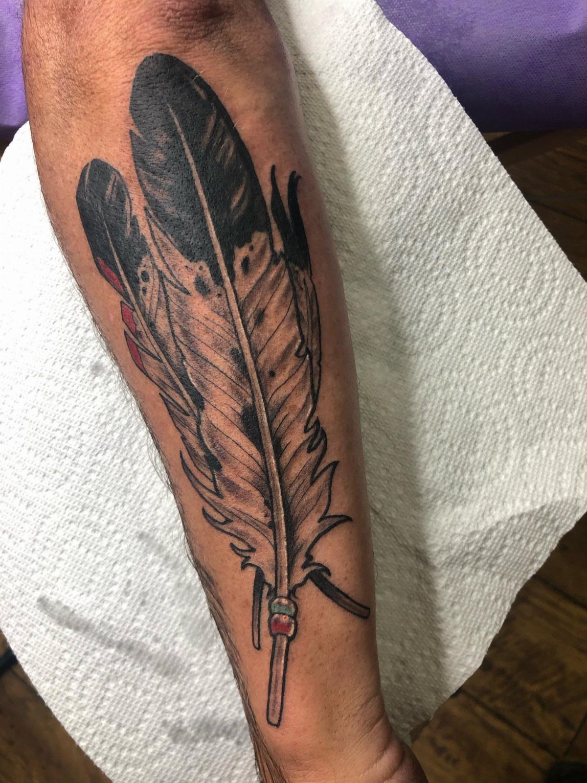 Feather tattoo on a forearm resting on a white paper towel.