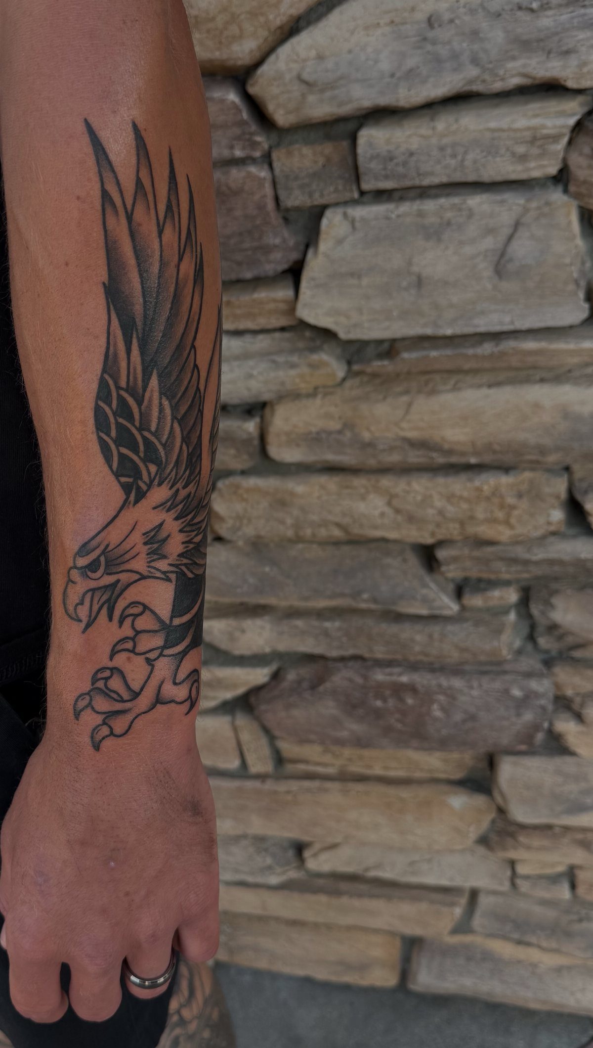 Eagle tattoo on a man's forearm and wrist against a stone wall