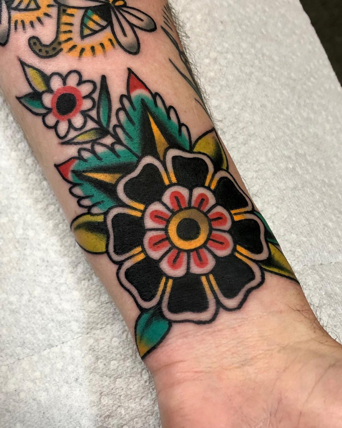 Traditional style flower tattoo on a person's wrist with bold black and red ink.