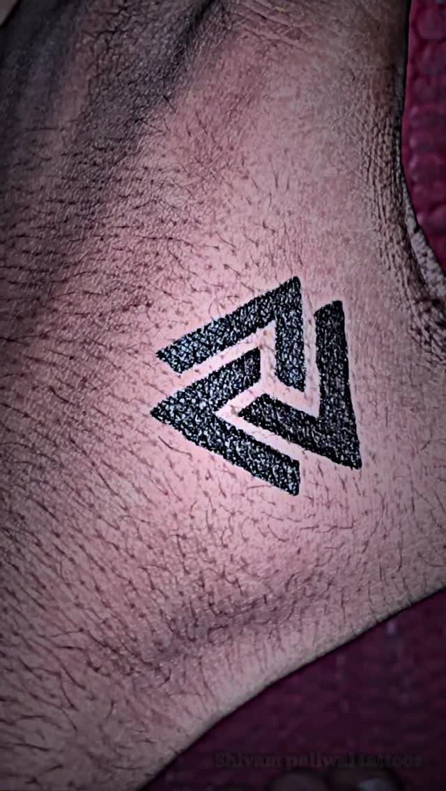 Geometric tattoo of three interlocking black triangles on a person's hairy wrist skin.