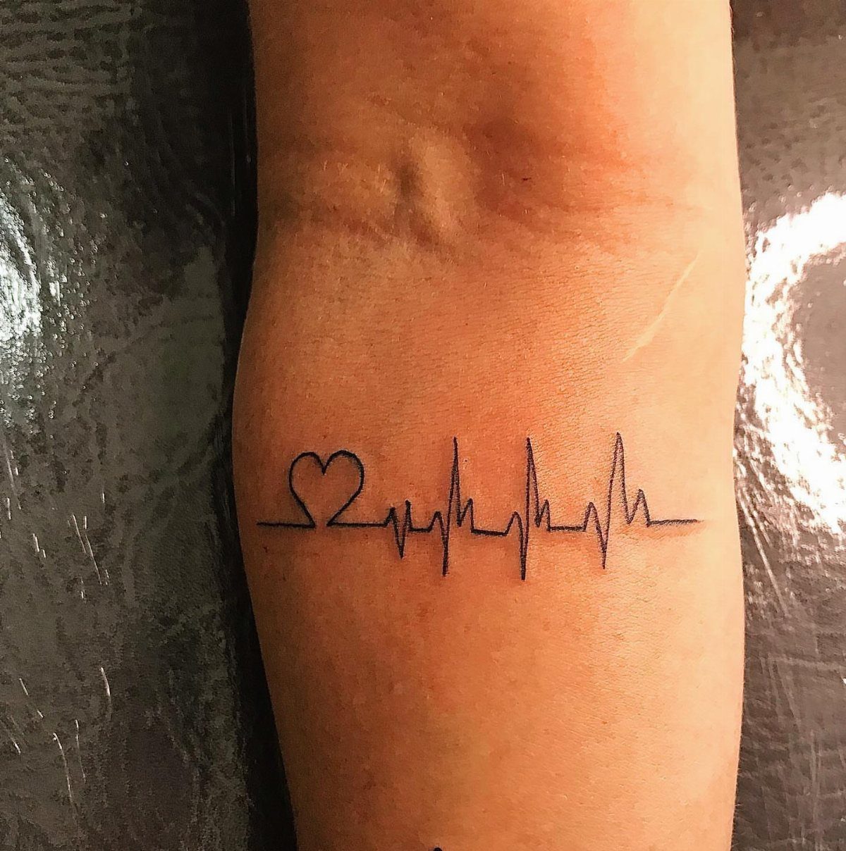 Heartbeat line tattoo with a small heart on a person's inner wrist.