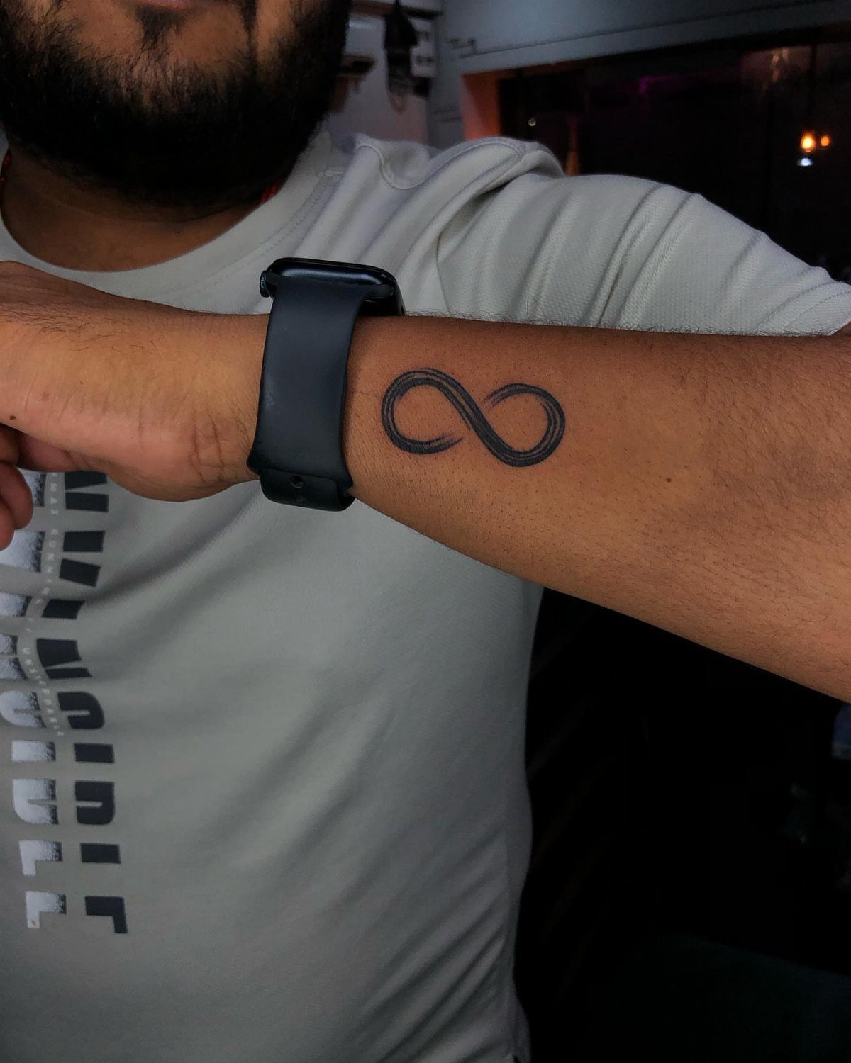 Infinity symbol tattoo on a man's wrist next to a black smartwatch