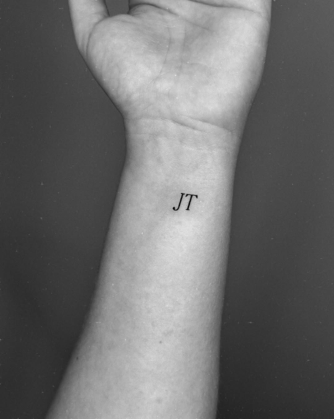 Inner wrist with a small black ink tattoo of the initials JT