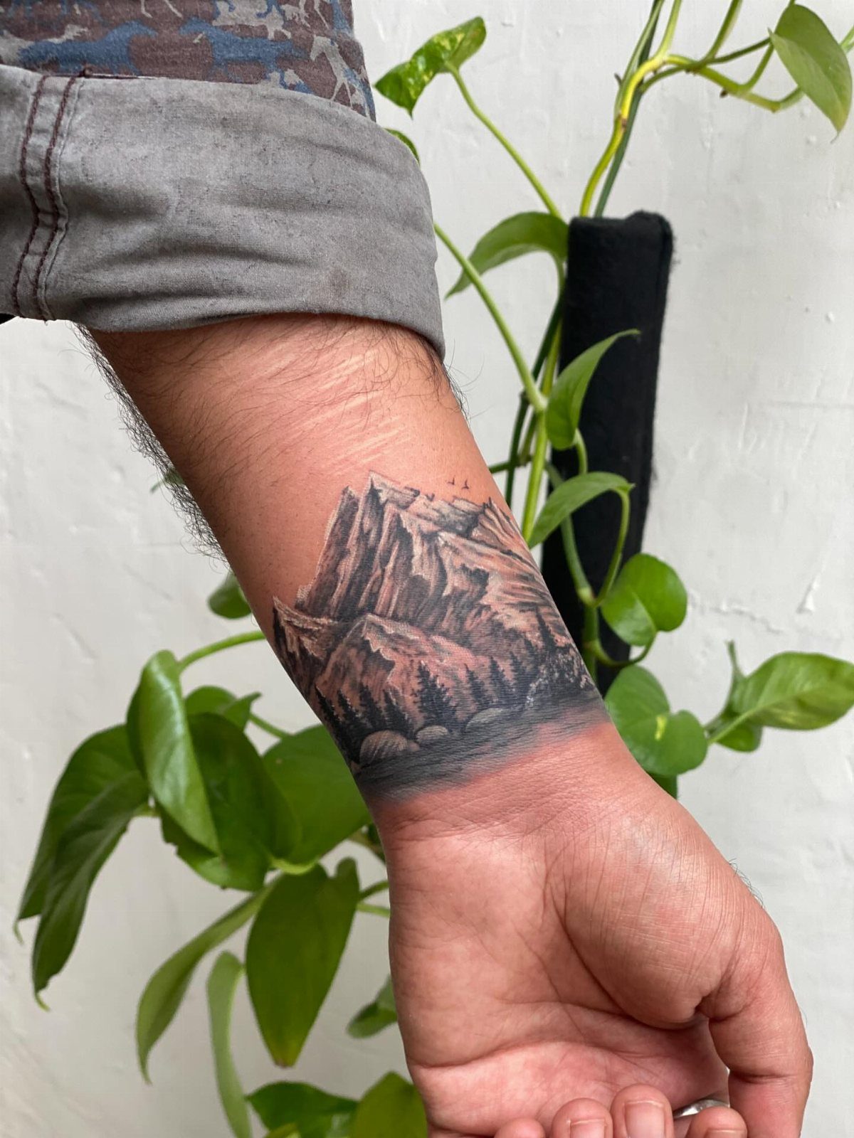 Mountain range tattoo on a man's wrist with a forest and grey shading.