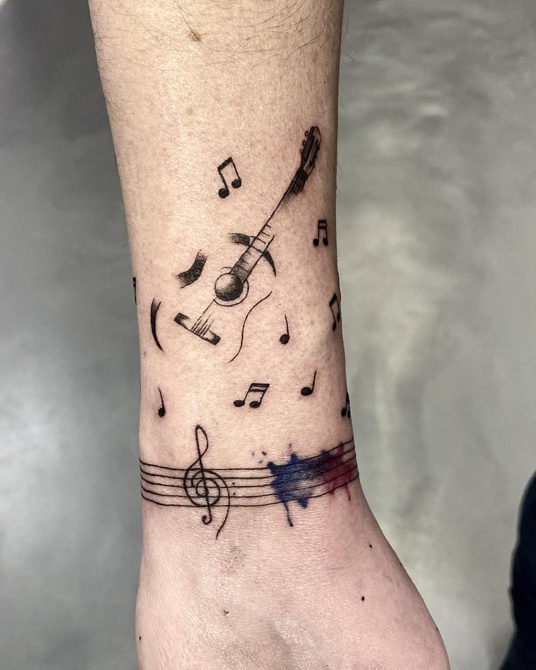 Wrist tattoo featuring a guitar, musical notes, and a treble clef on a staff.