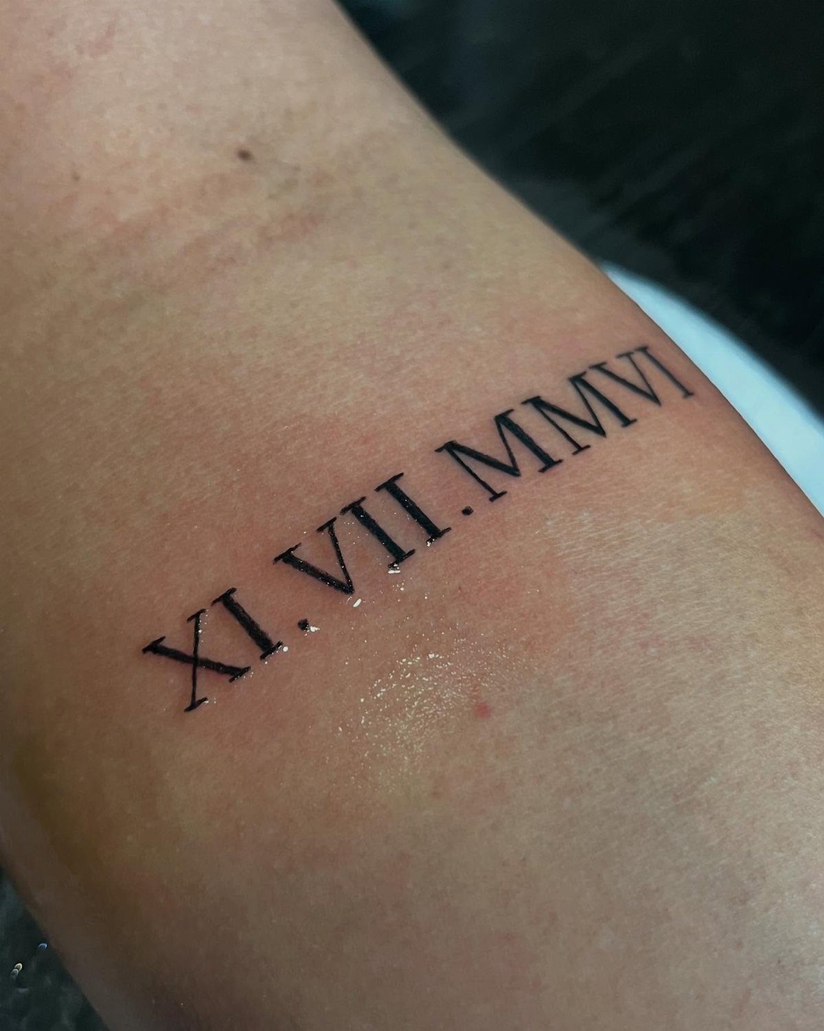 Roman numeral tattoo on a wrist reading XI.VII.MMVI in black ink