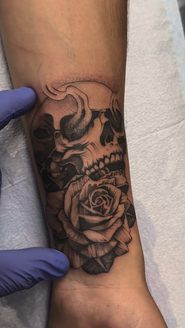 Skull and rose tattoo on a man's wrist and forearm in black and grey ink.