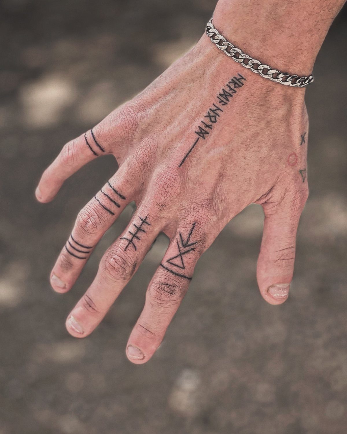 Man's hand with Viking rune tattoos on the back and bands on fingers.