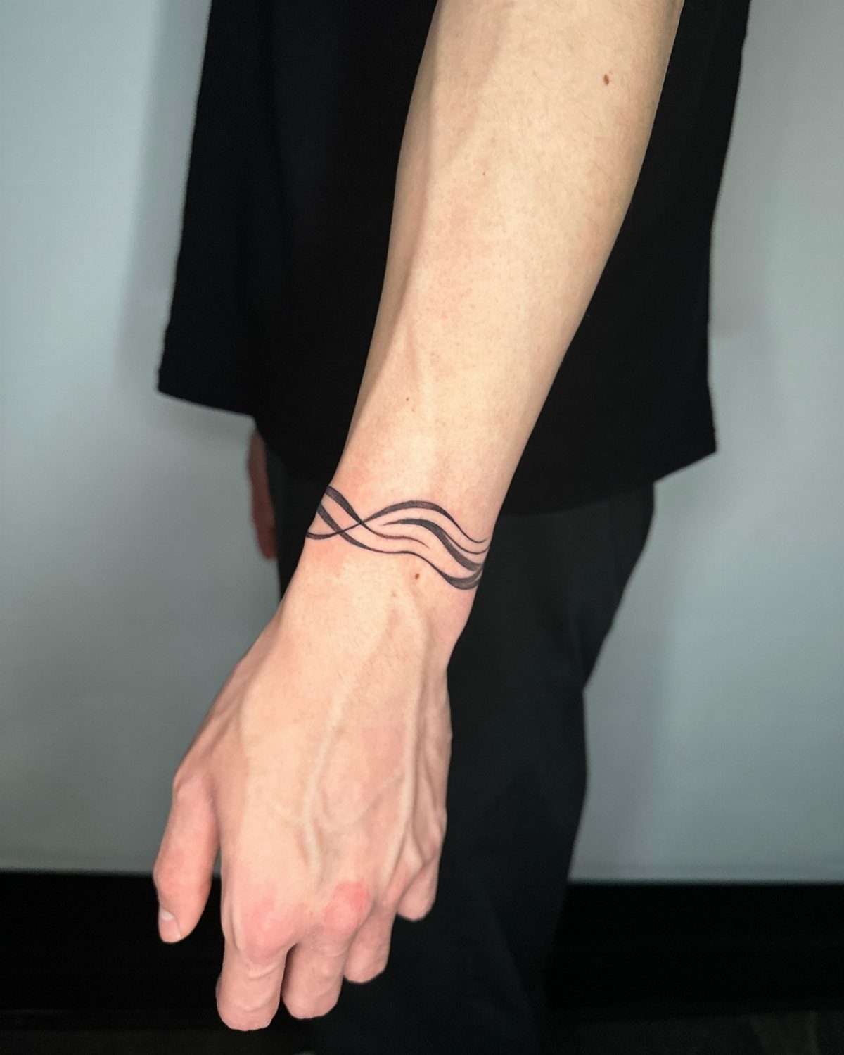 Wrist with a black ink tattoo of three parallel wavy lines wrapping around.
