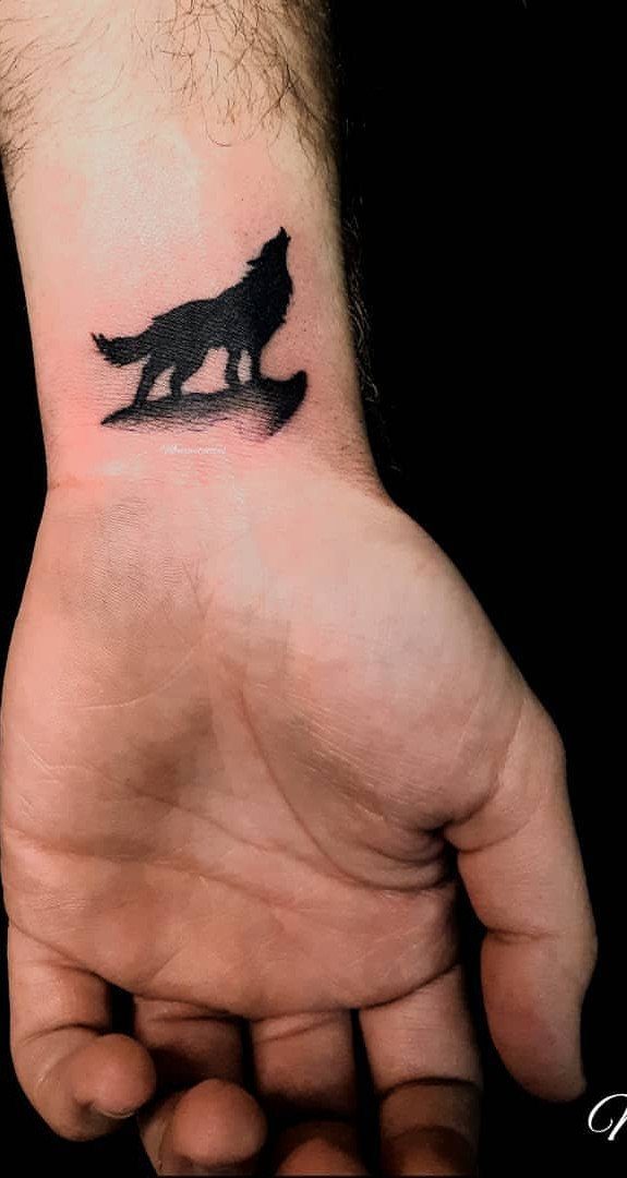 Howling wolf silhouette tattoo on the inner wrist of a man's arm.
