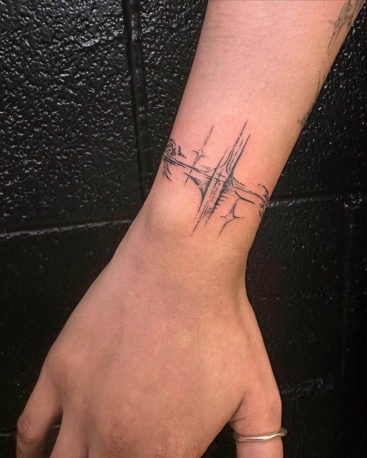 Abstract linear tattoo on a person's wrist against a black textured wall