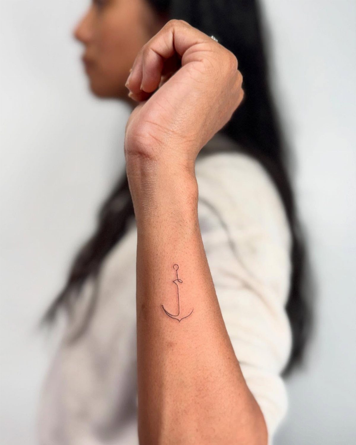 Small minimalist black ink anchor tattoo on a woman's inner wrist.