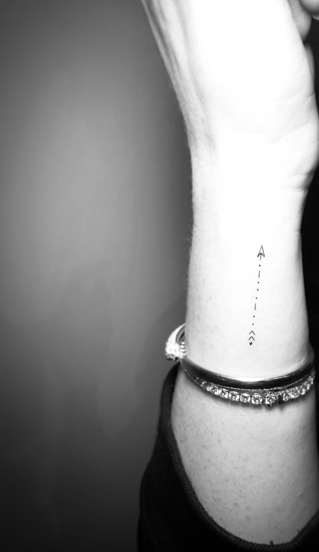 Small black arrow tattoo with a dotted line on a person's inner wrist.