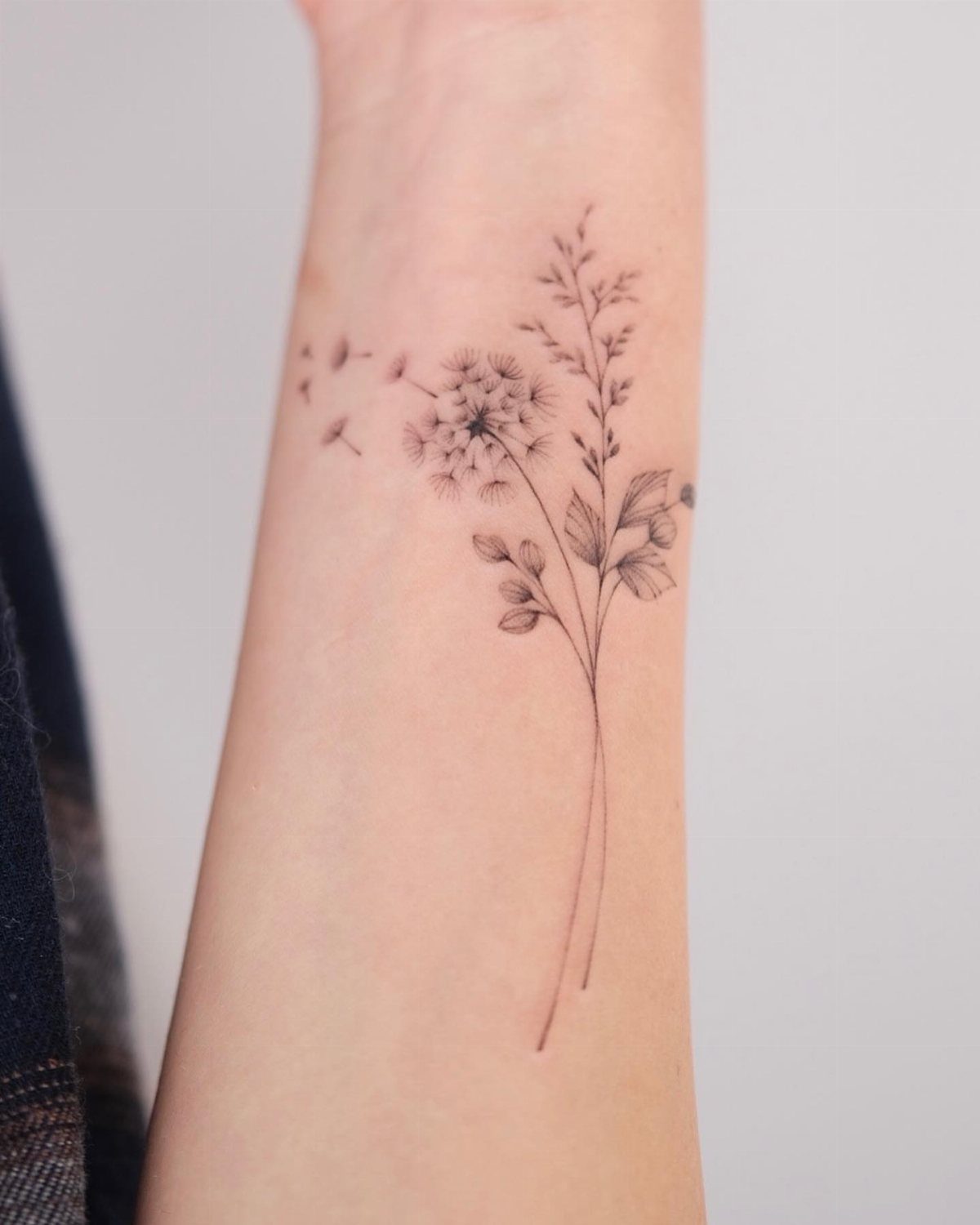 Dandelion tattoo on a wrist with seeds blowing in the wind.