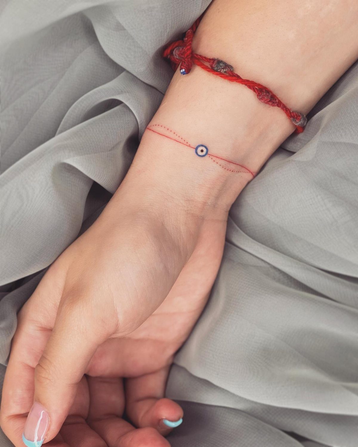 Evil eye tattoo on a wrist with a thin red line and bracelet.