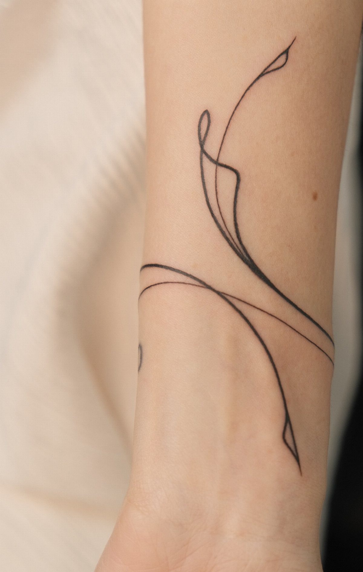 Minimalist line art tattoo with flowing black curves on a person's inner wrist.