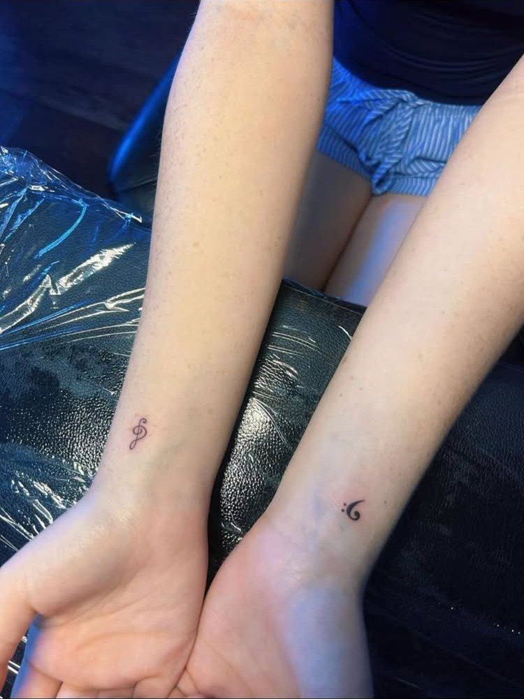 Two inner wrists each featuring a small black music note tattoo.